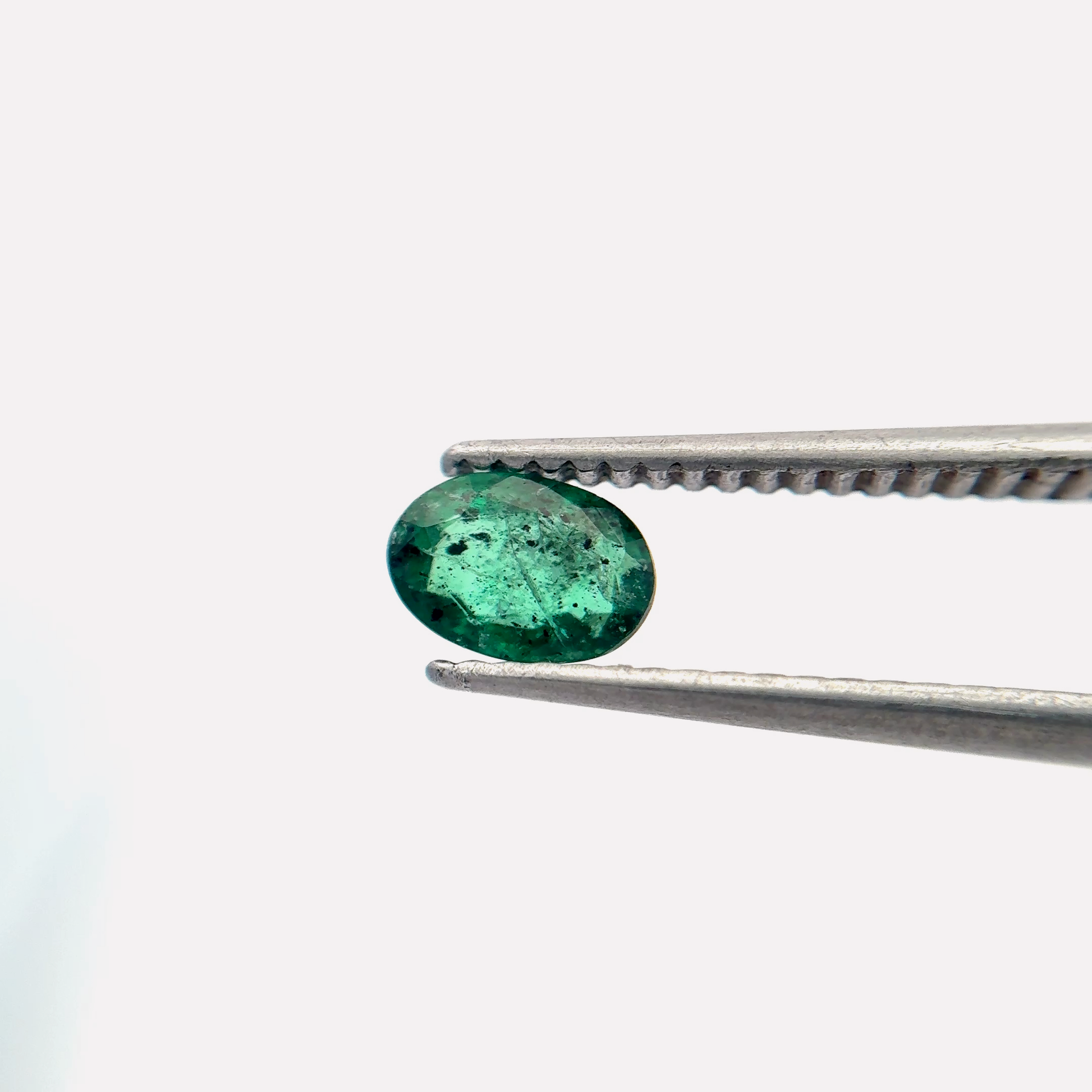 Green emerald held by tweezers on a white background
