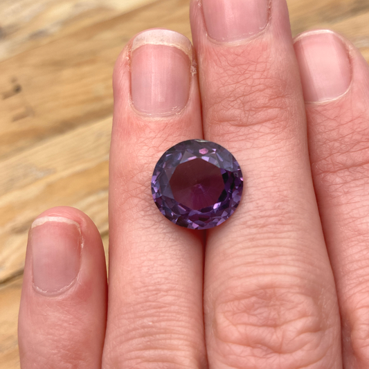 Purple gemstone on a finger against a blurred natural background