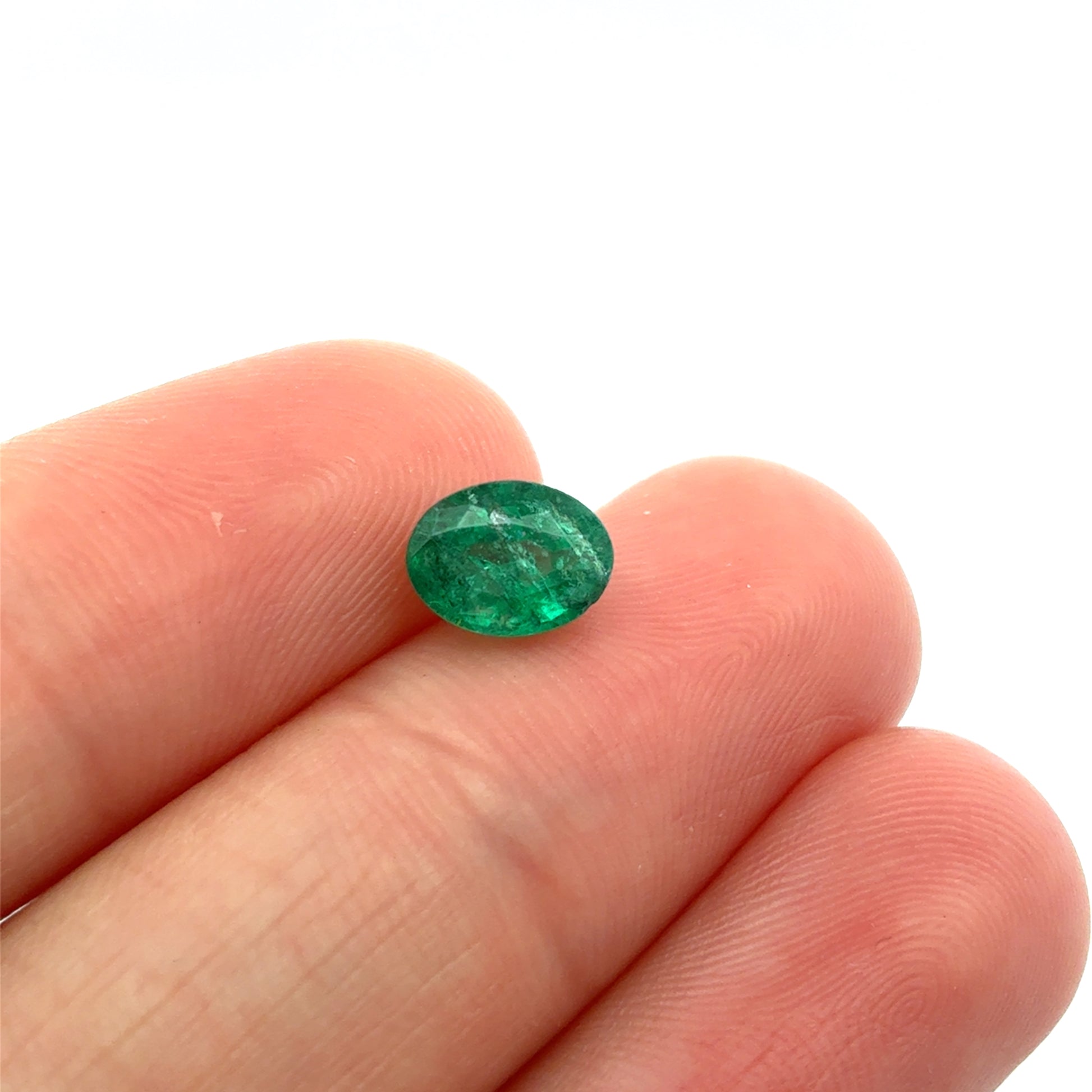 Green gemstone held between fingers on a white background