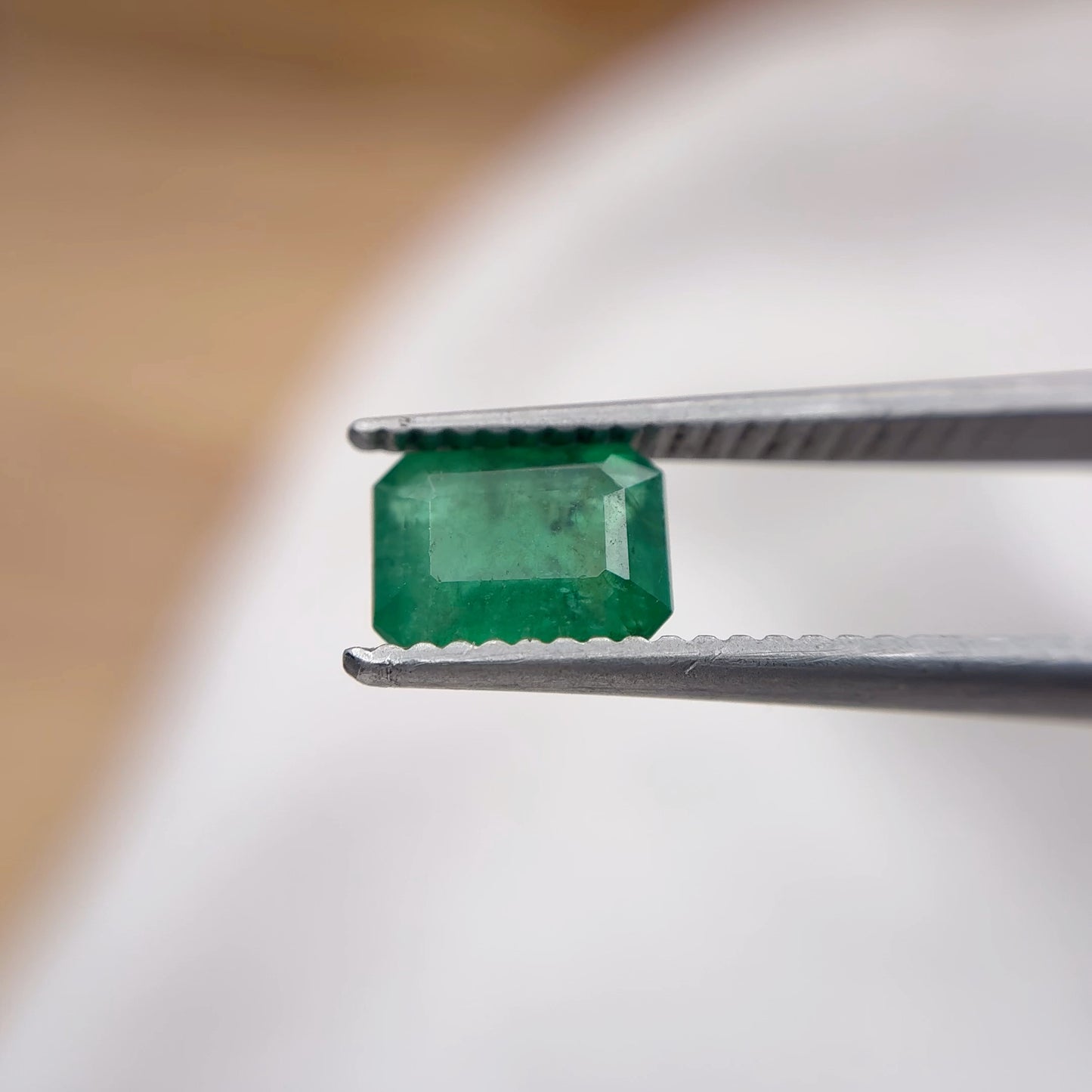 Green emerald held between tweezers against a blurred background