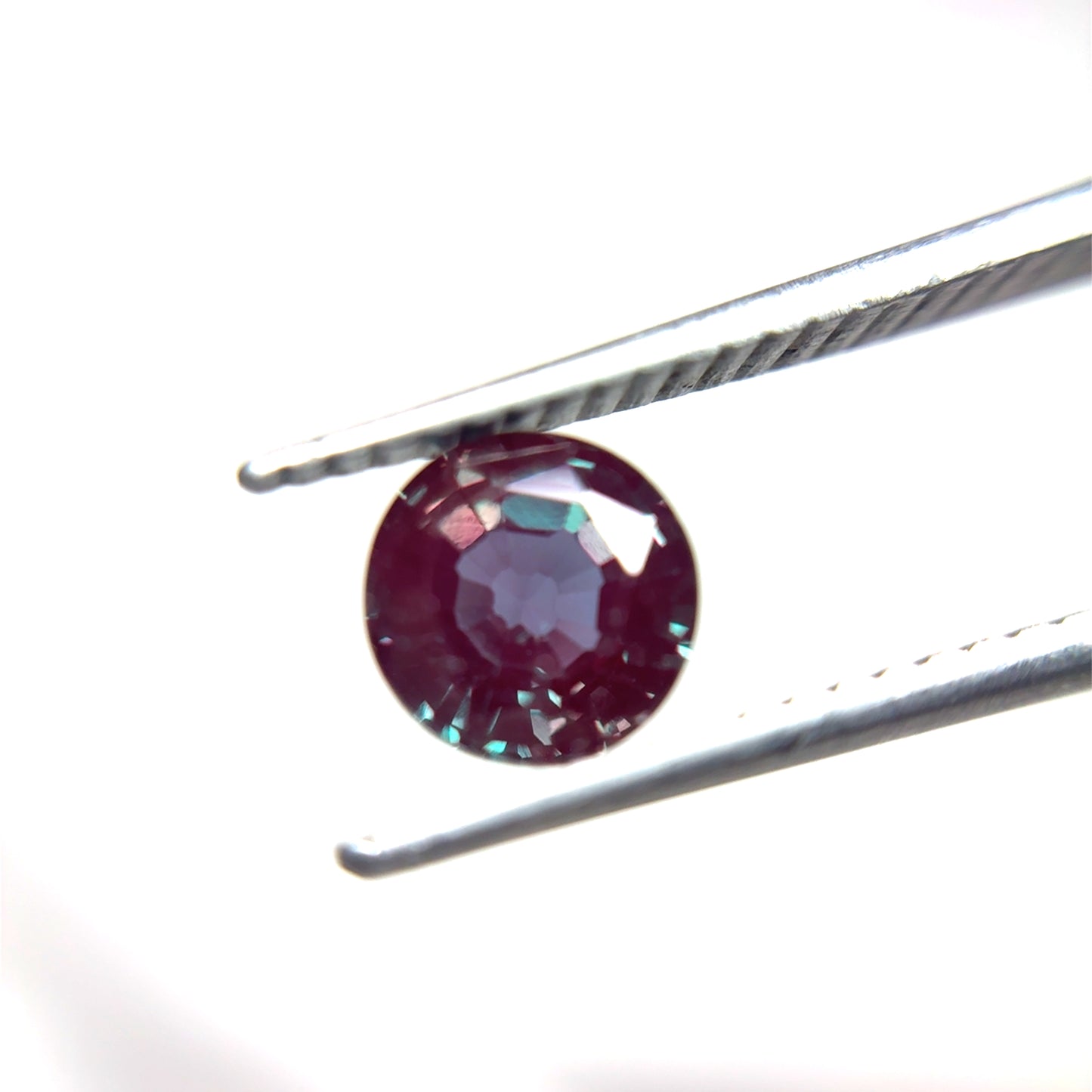 Round Purple and green lab created alexandrite held by tweezers on a white background