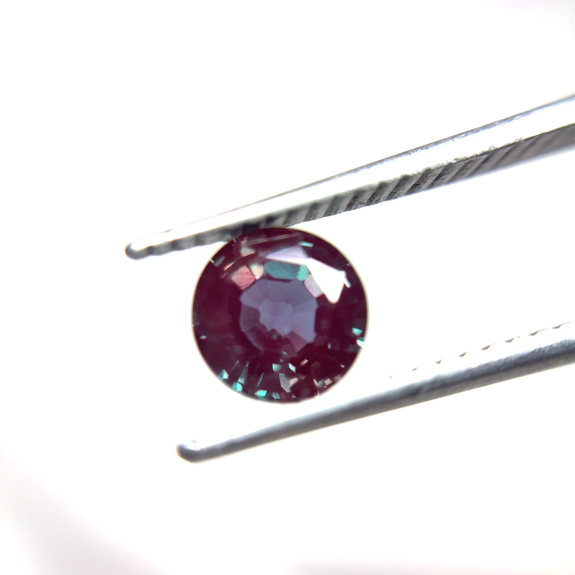 Round Purple and green lab created alexandrite held by tweezers on a white background