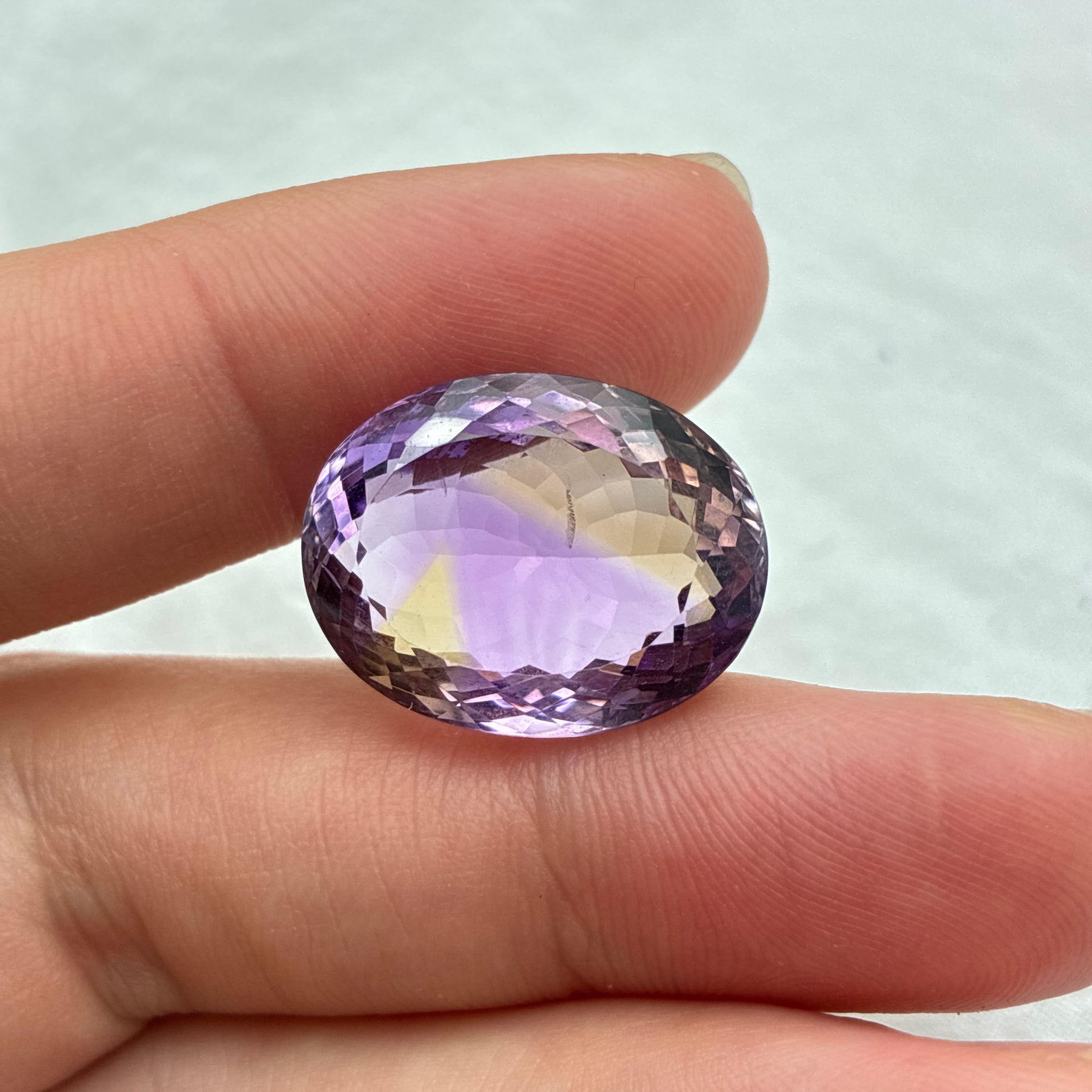 Purple and yellow ametrine held between fingers against a light background