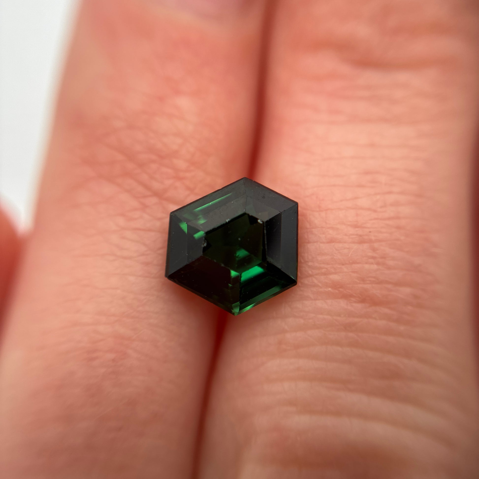 Green gemstone (Tourmaline)  held between fingers against a neutral background