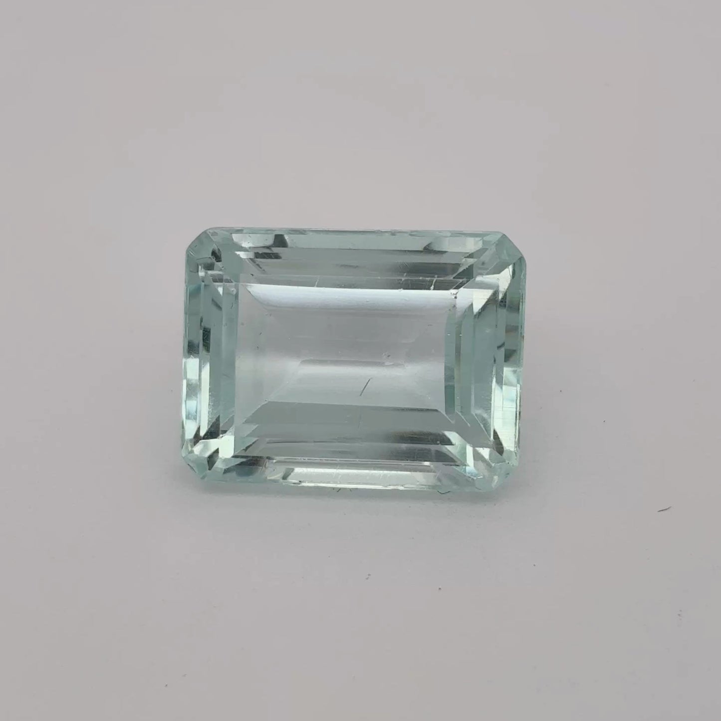 Rectangular greenish-blue gemstone on a gray background