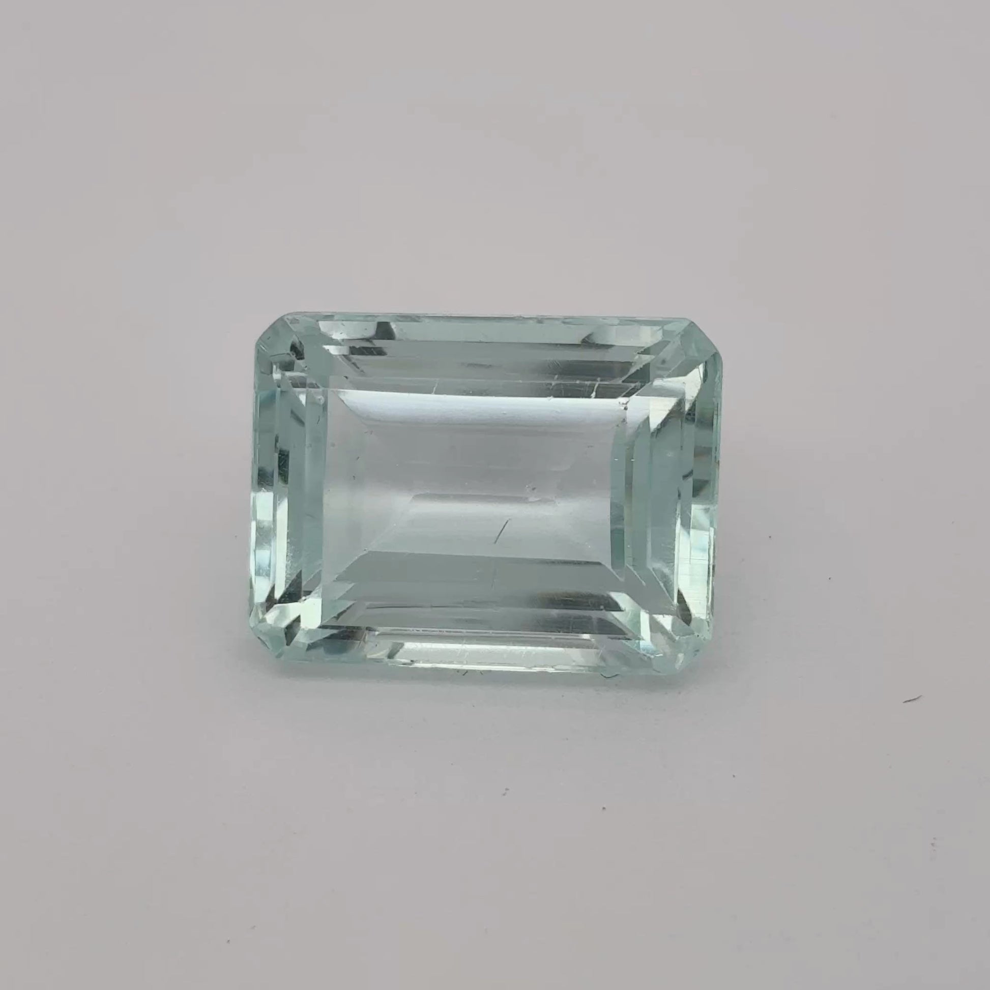 Rectangular greenish-blue gemstone on a gray background